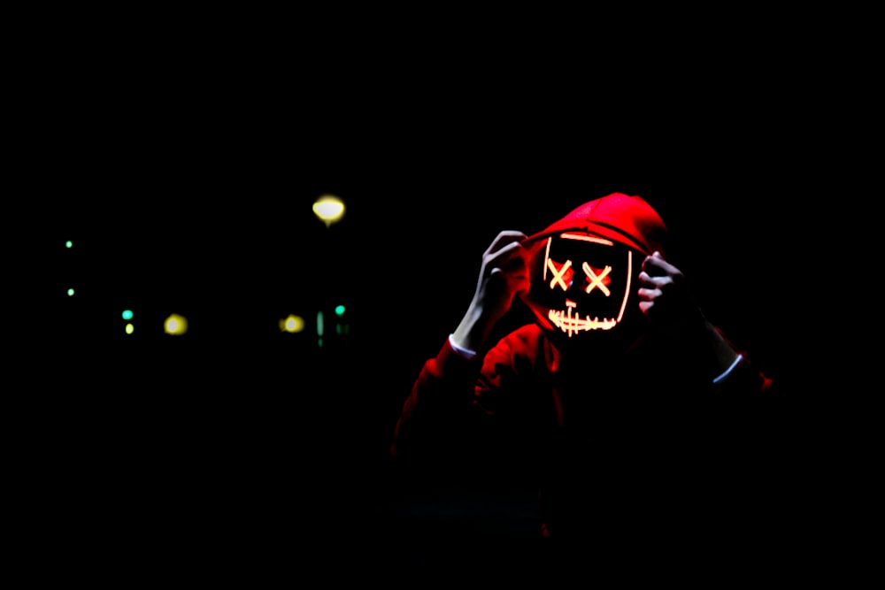 person wearing hoodie and neon mask
