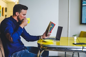 man drinking on yellow cup while reading book