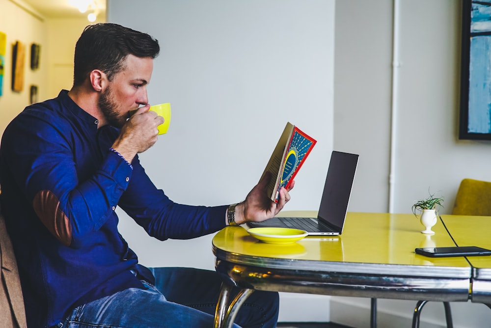 Hombre bebiendo en una taza amarilla mientras lee un libro