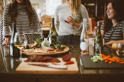 two woman standing beside woman sitting in front of table dinner teams background