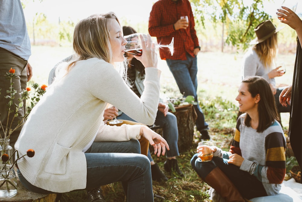 woman sitting near people while drinking alcohol