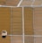 Aerial view of a series of rectangular agricultural fields with varying shades of brown and beige. A solitary wooden structure is situated in one of the fields, casting a shadow on the ground. The fields are divided by narrow pathways or irrigation channels.