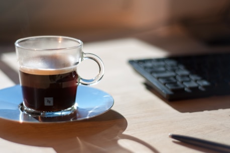 A sleek coffee tumbler resting on a wooden desk with morning sunlight streaming in.