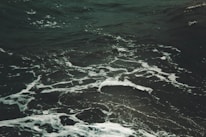 Dark ocean water with visible white foamy waves swirling in various directions, creating a textured surface on the sea.
