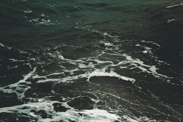 Dark ocean water with visible white foamy waves swirling in various directions, creating a textured surface on the sea.