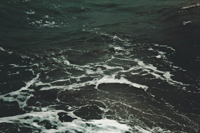 Dark ocean water with visible white foamy waves swirling in various directions, creating a textured surface on the sea.