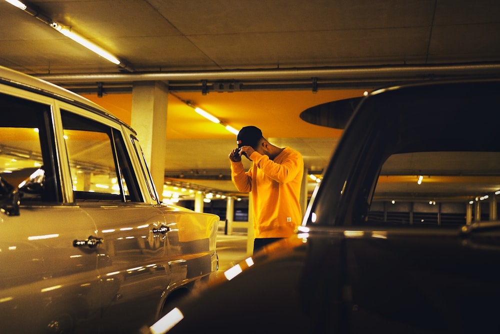 man holding cap standing between car on parking lot