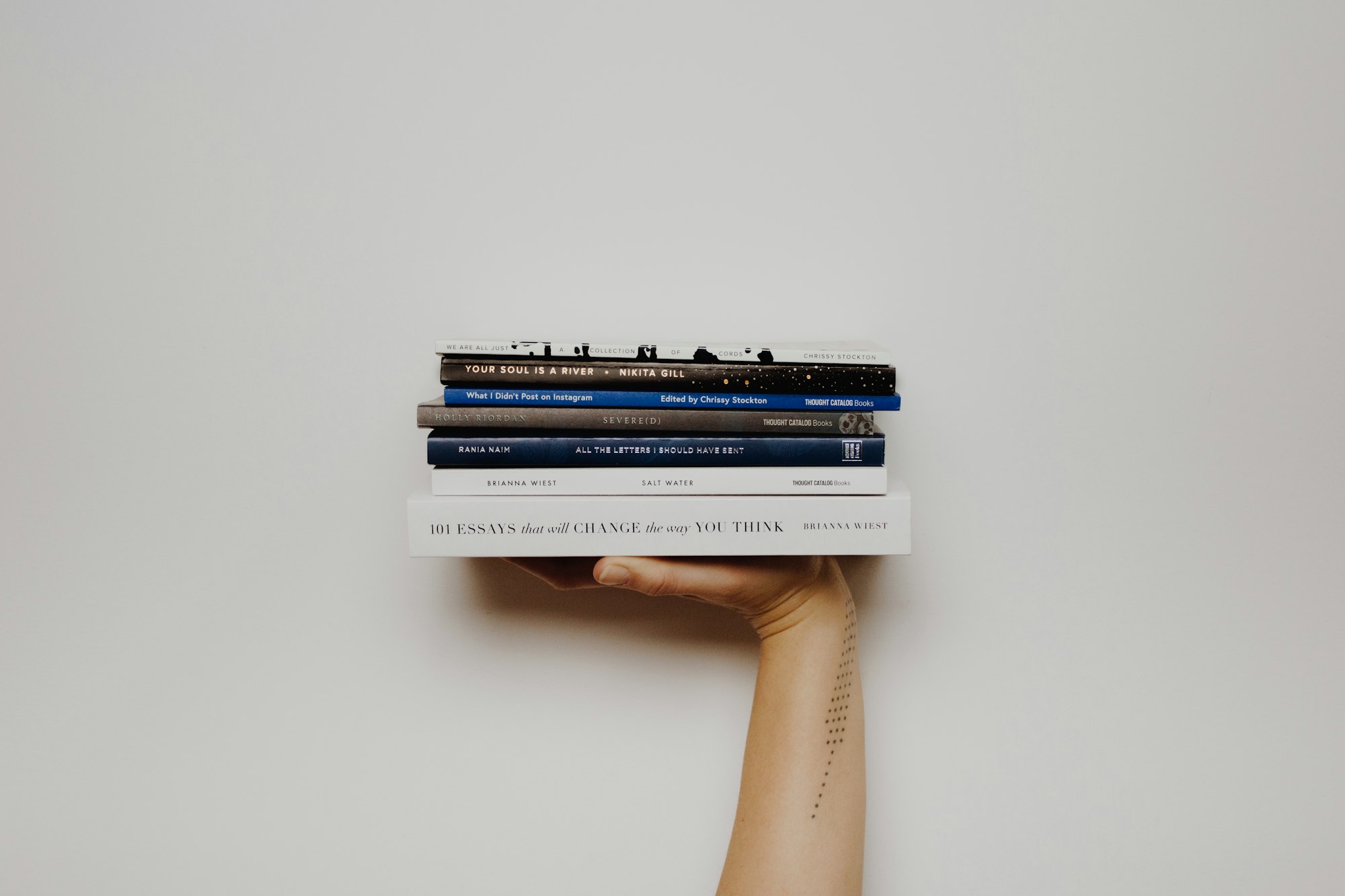 Woman with a tattoo holding up a stack of books.