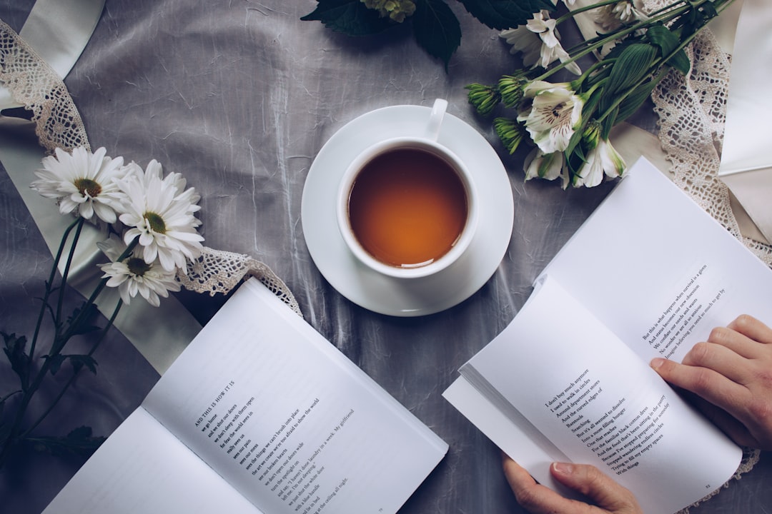 Woman reading a book with tea and flowers.