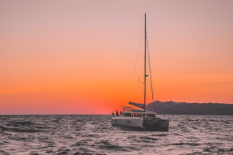A sailboat gently gliding past a beautiful sunset on the horizon.