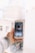 A hand is holding a smartphone with an application open on the screen. The background appears to be a blurred cityscape with tall buildings. The smartphone screen displays profile information and various statistics relating to the profile.