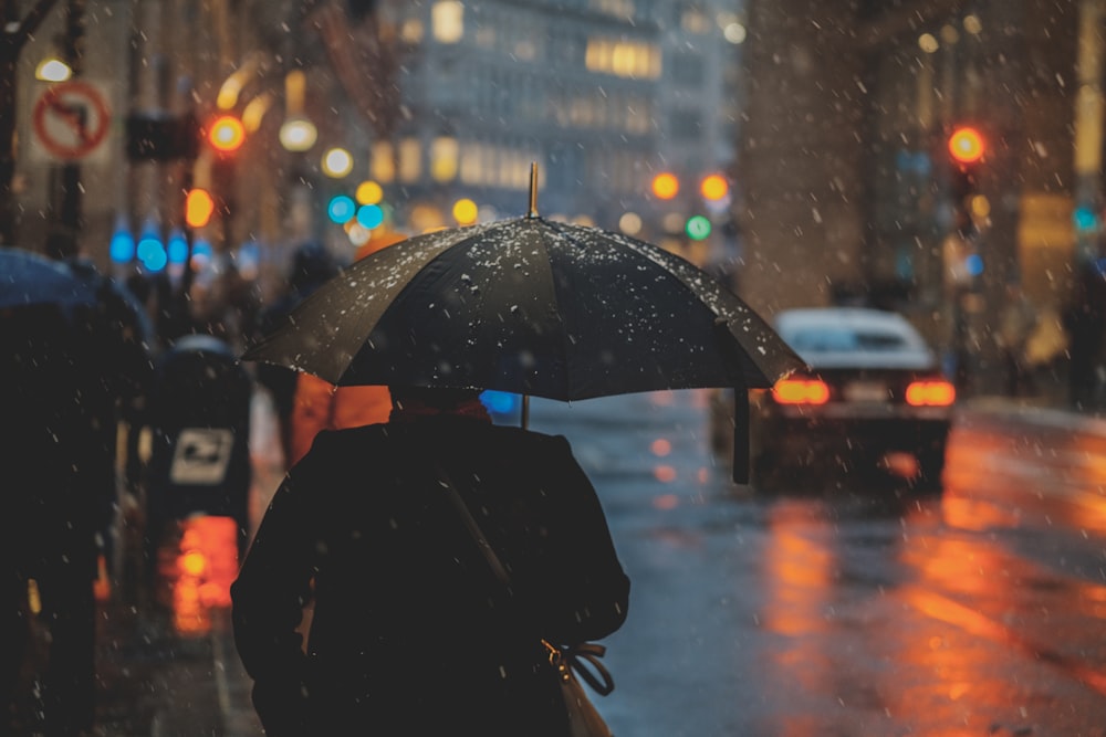 雨が降っているときに傘をさして通りを歩いている人、近くに車がいる