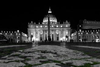 Evening view of St. Peter's Square with soft lights highlighting the columns and the basilica.