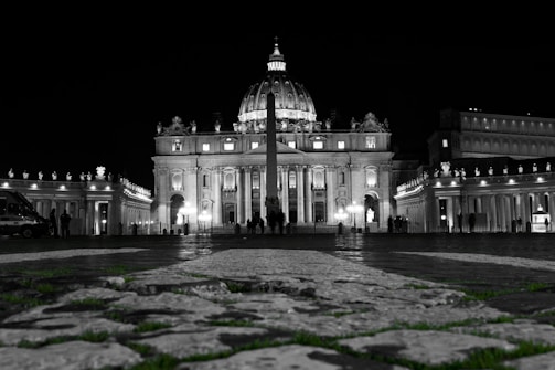 Evening view of St. Peter's Square with soft lights highlighting the columns and the basilica.