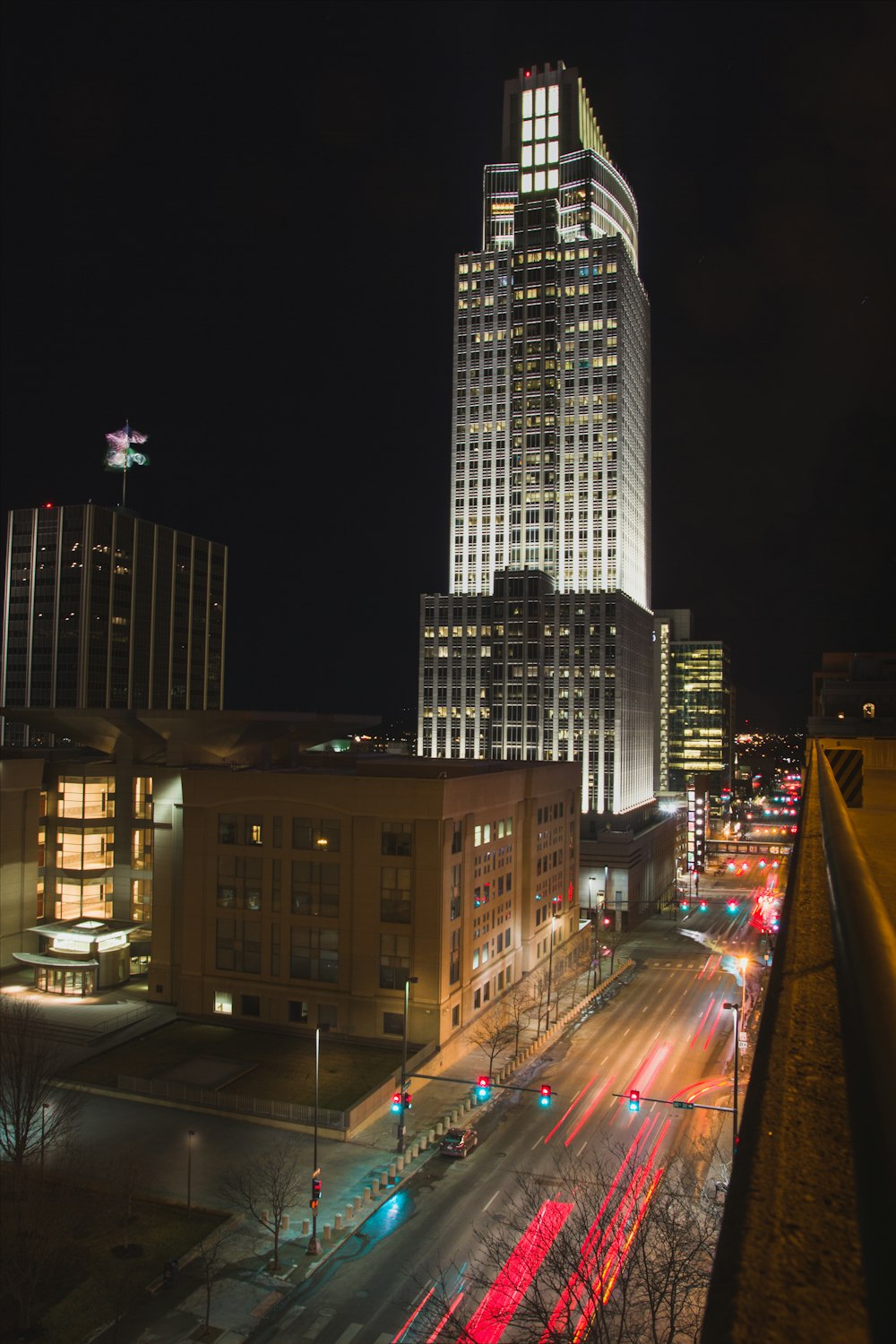 Photographie en accéléré de véhicules se déplaçant sur la route près d’un immeuble de grande hauteur sous un ciel nocturne noir