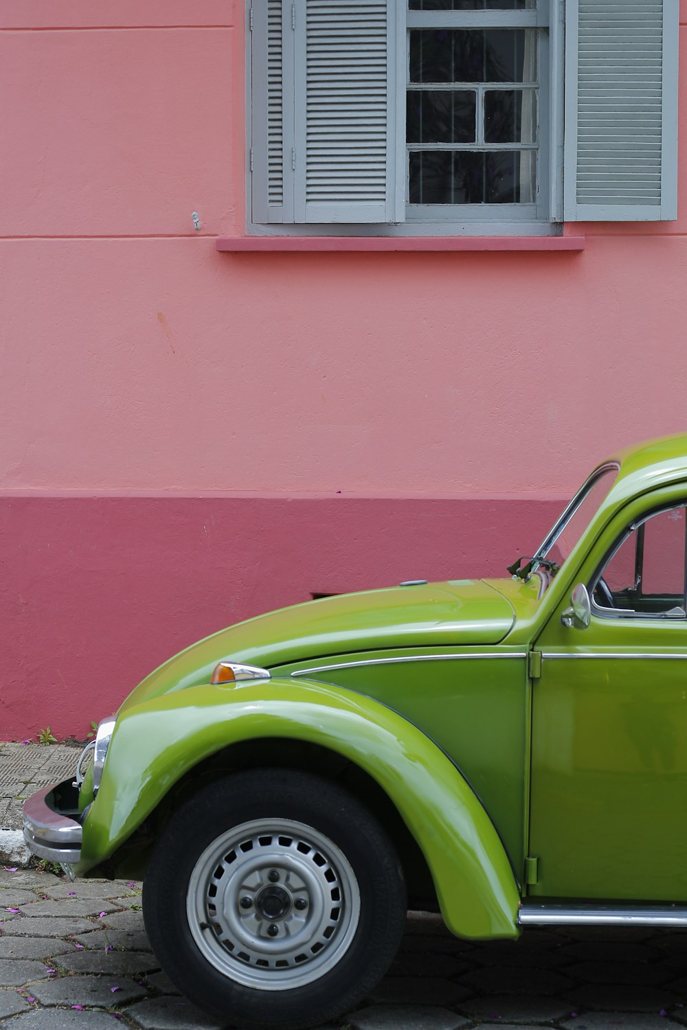 green Volkswagen beetle beside of pink building