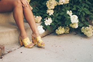 woman sitting on brown stair beside yellow and white flowers