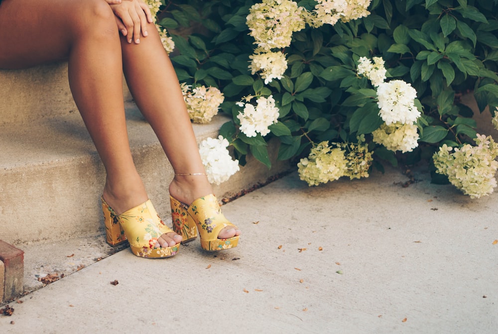 Mujer sentada en una escalera marrón junto a flores amarillas y blancas