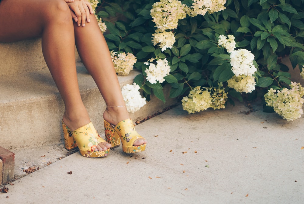woman sitting on brown stair beside yellow and white flowers
