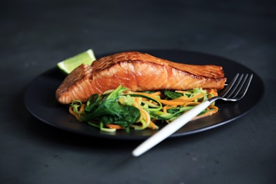 grilled fish, cooked vegetables, and fork on plate meal zoom background