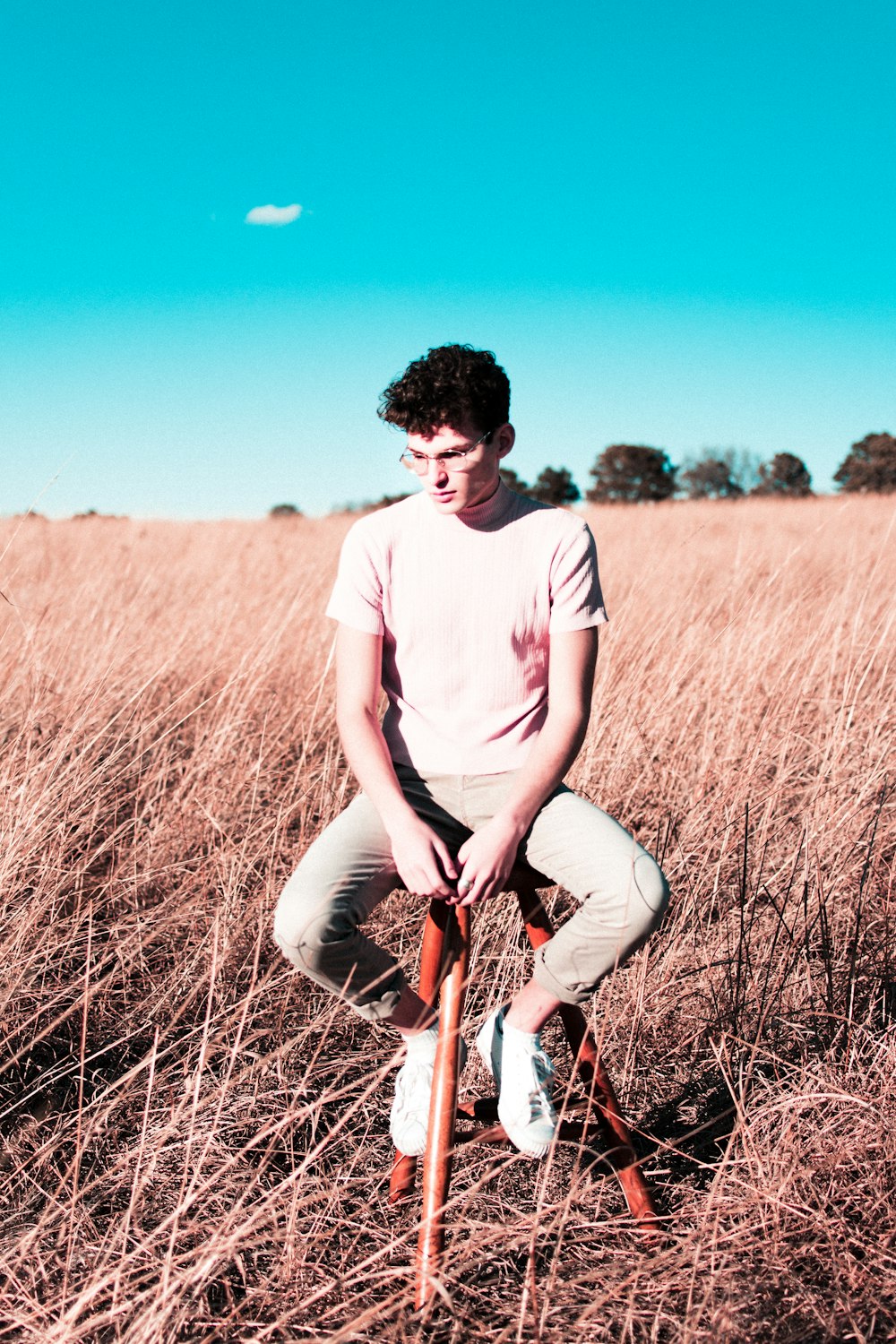 man sitting on red stool on brown field grass during daytime