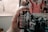 A hand holds a bottle of Starbucks Cold Brew Coffee, labeled with the mermaid logo and text indicating it is a premium coffee drink. The background is slightly blurred, showing a room with various objects including blurry images of people.