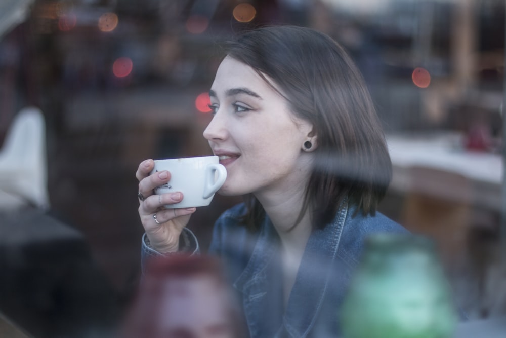 mujer sosteniendo una taza de té de cerámica blanca