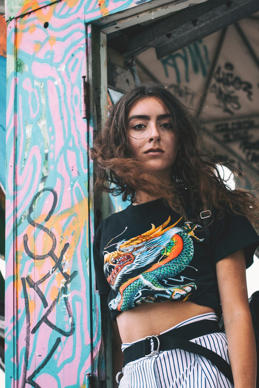 Mujer con camiseta gráfica de dragón apoyada en el marco de la puerta