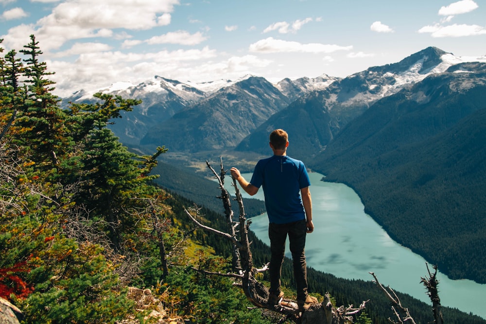 man standing on tree overlooking the lake surround by mountains