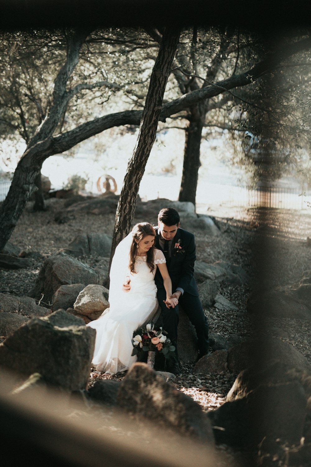 groom and bride sitting on rock holding hands