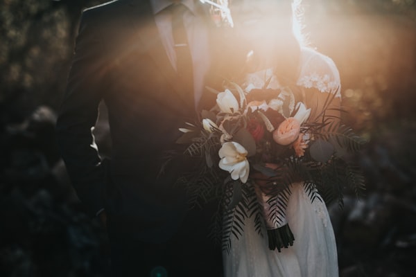 Un hombre y una mujer vestidos de novios con un ramo.