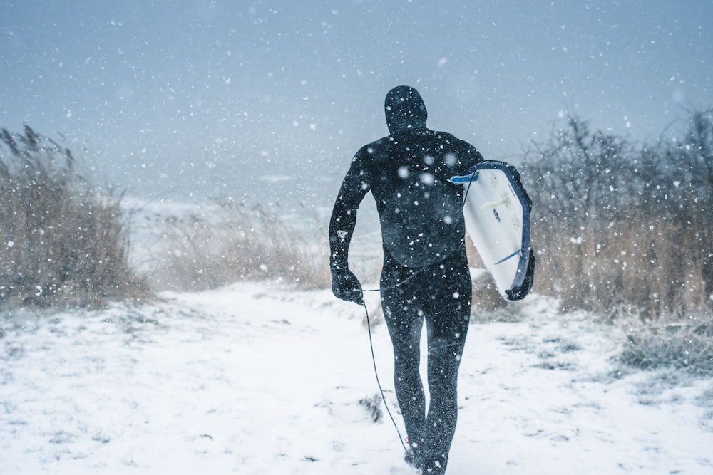 man carrying surfboard walking on snow