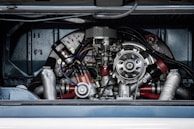 A detailed view of a complex mechanical engine, featuring various metallic components, tubes, and wires. The engine is housed within a vehicle compartment, showcasing its intricate design and craftsmanship.