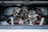 A detailed view of a complex mechanical engine, featuring various metallic components, tubes, and wires. The engine is housed within a vehicle compartment, showcasing its intricate design and craftsmanship.