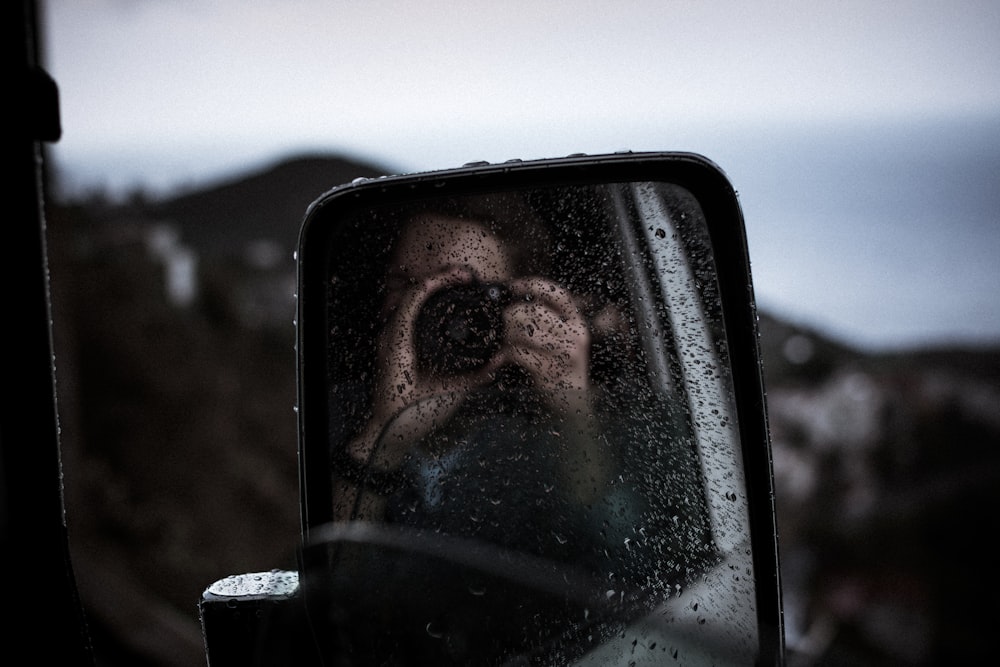 Reflexion der Person, die die DSLR-Kamera am Seitenspiegel des Fahrzeugs verwendet