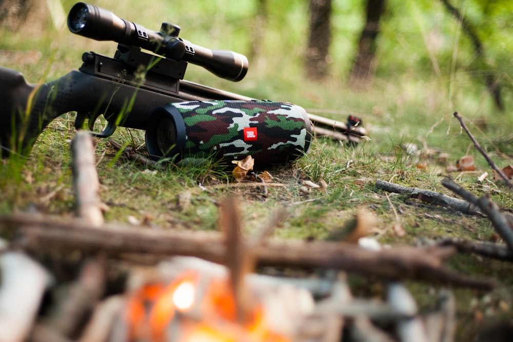 black sniper rifle beside green, black, and white camouflage JBL portable speaker