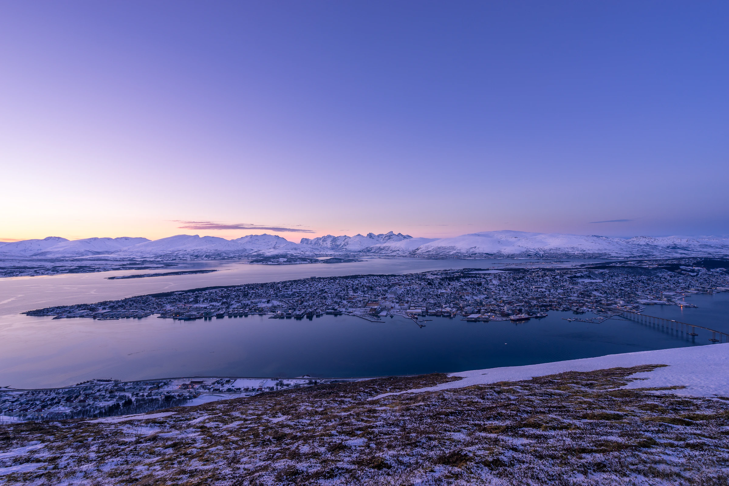 Kota Tromso di tepi fjord dengan pegunungan bersalju.