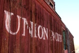 Weathered wooden panels form the side of a vintage train car with 'Union Pacific' painted in faded white letters. The red paint on the wood is peeling, adding a rustic and historical feel.
