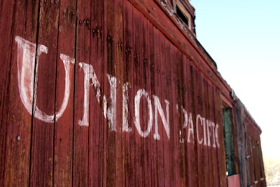 Weathered wooden panels form the side of a vintage train car with 'Union Pacific' painted in faded white letters. The red paint on the wood is peeling, adding a rustic and historical feel.