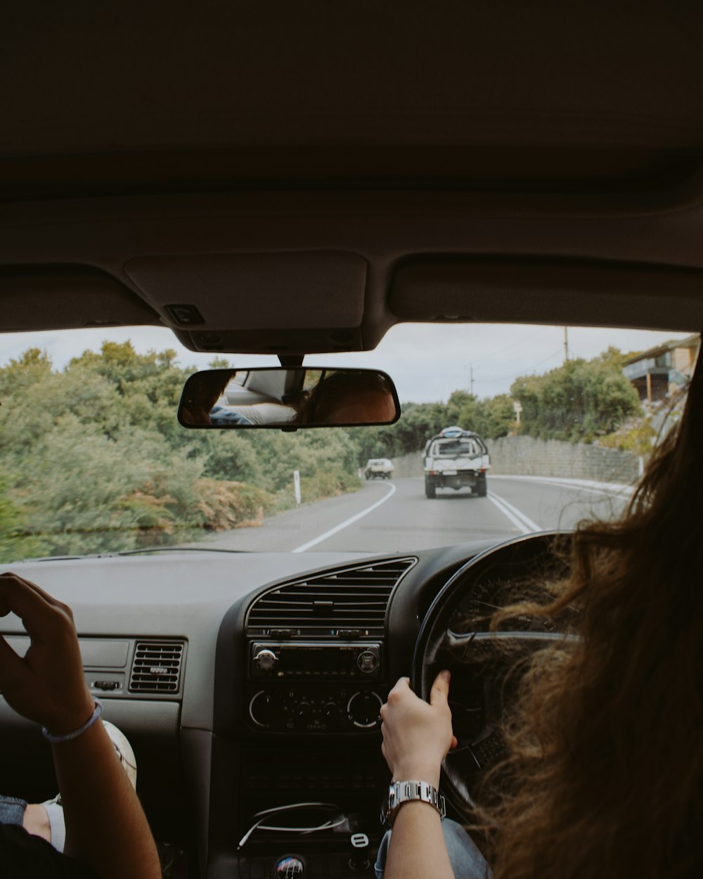 woman driving car on tree lined road during daytime