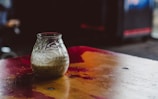 Close-up of golden woodpressed oil pouring into a glass jar on a rustic wooden table.
