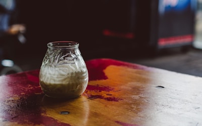 Golden jar of bilona a2 desi cow ghee with a wooden spoon resting beside it on a rustic wooden table.