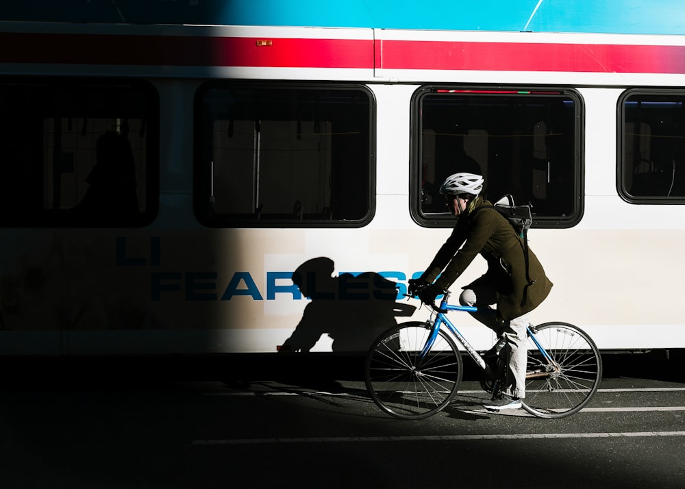 Persona monta en bicicleta urbana en carretera asfaltada al lado del autobús blanco