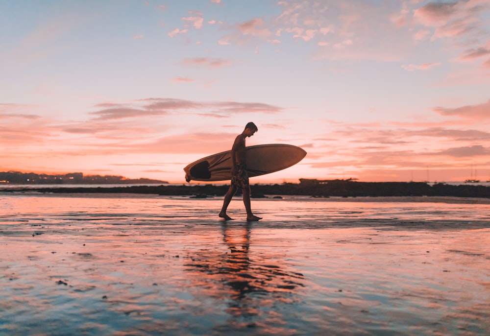 homem segurando prancha de surf caminhando perto da costa