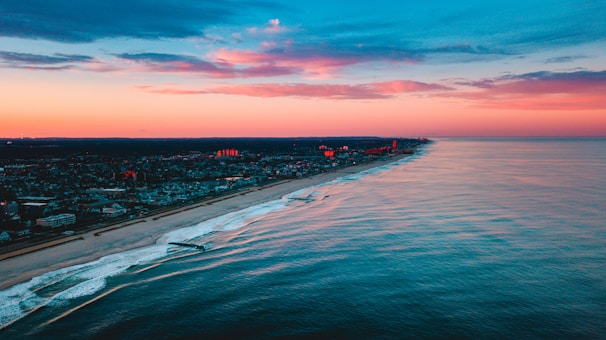 A sweeping aerial shot of a pastel-colored coastline at sunset, captured by a drone.