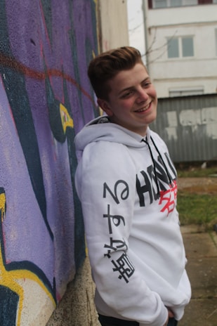 A woman in casual streetwear leaning against a graffiti-covered wall, smiling naturally.