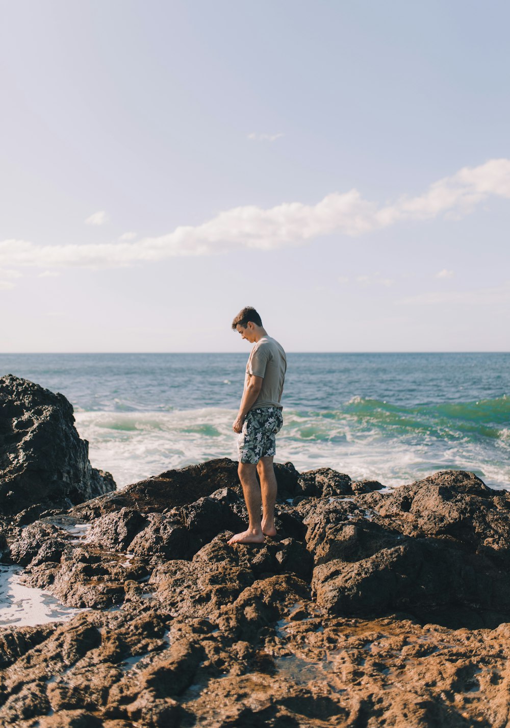 uomo in piedi sull'isola rocciosa accanto alla spiaggia