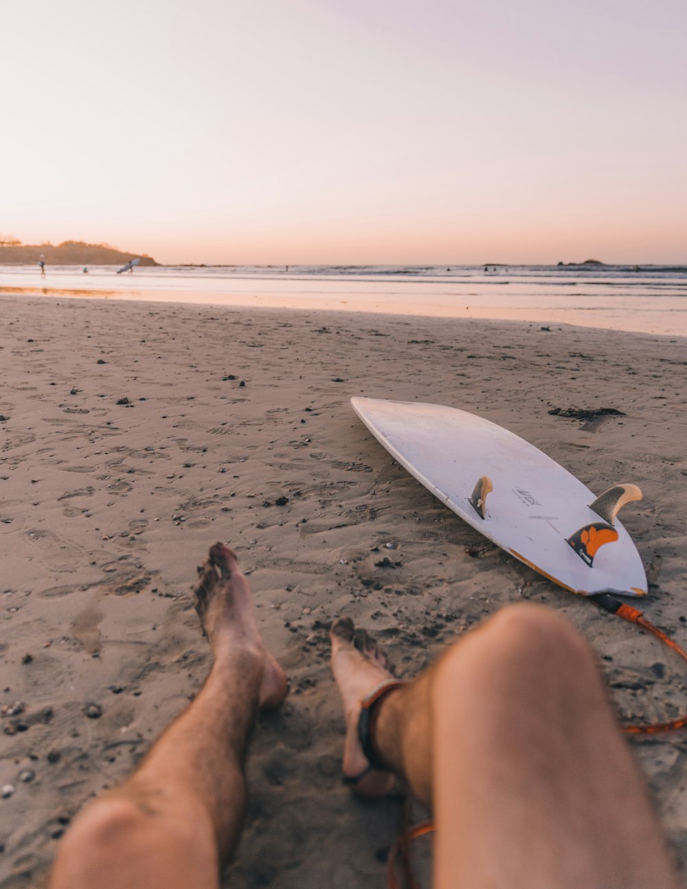 person sitting on seashore near surfboard in front sea