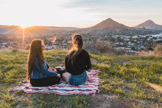 two women having picnic facing mountain and buildings during golden hour in San Luis Obispo United States