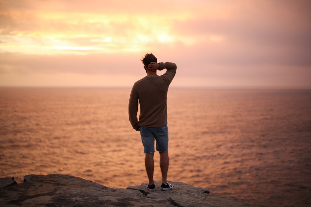 man standing on rock near seashore during sunset
